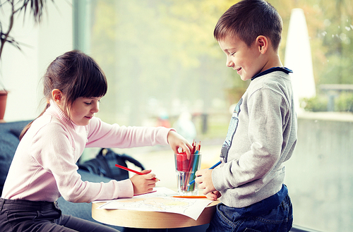 childhood, leisure, friendship and people concept - happy little girl and boy drawing and coloring picture with pencils at home