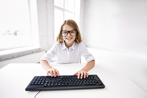 education, children, technology and people concept - little student girl in black eyeglasses with computer keyboard at school
