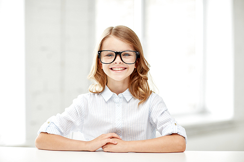 education, vision, elementary school, learning and people concept - happy smiling girl in eyeglasses sitting at table