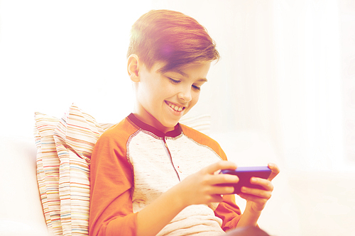 leisure, children, technology, internet communication and people concept - smiling boy with smartphone texting message or playing game at home