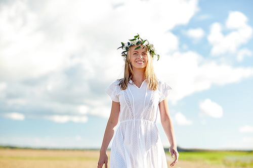 happiness, nature, summer holidays, vacation and people concept - happy smiling young woman or teenage girl in wreath of flowers and white dress at countryside