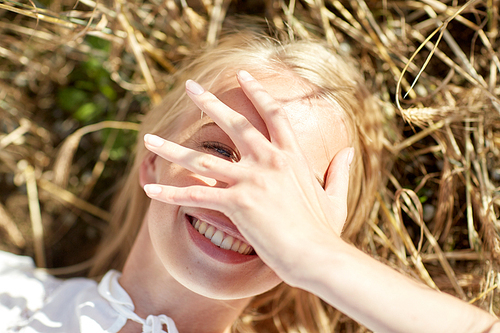 nature, summer holidays, vacation and people concept - close up of happy young woman lying on cereal field and covering face by hand