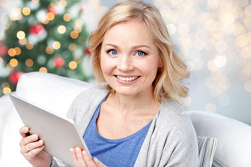 people, christmas, technology and internet concept - happy middle aged woman with tablet pc computer at home over holidays lights background