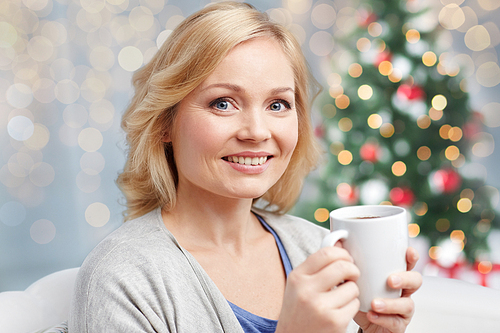 people, christmas, drinks and leisure concept - smiling woman with cup of tea or coffee at home over holidays lights background