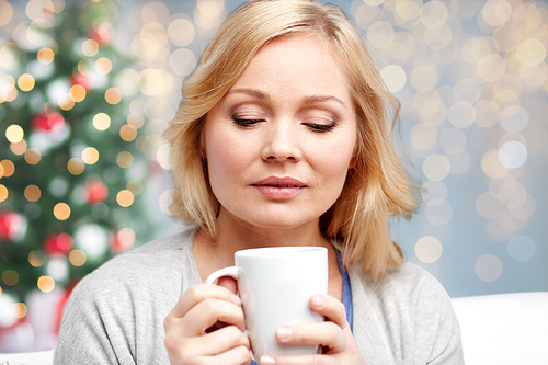 people, christmas, guesswork, drinks and leisure concept - woman with cup of tea or coffee at home over holidays lights background