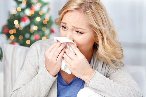healthcare, flu, christmas, and people concept - ill woman blowing nose to paper napkin