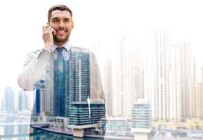 business, technology, communication and people concept - young smiling businessman calling on smartphone over dubai city background with double exposure effect
