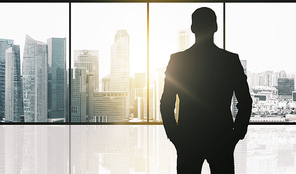 business and people concept - silhouette of businessman over office window and singapore city skyscrapers background and sun light