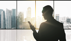business and people concept - silhouette of businessman with smartphone over office window and singapore city skyscrapers background and sun light