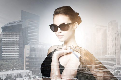 sale, fashion, people and luxury concept - happy beautiful young woman in black sunglasses with shopping bags over dubai city with double exposure background