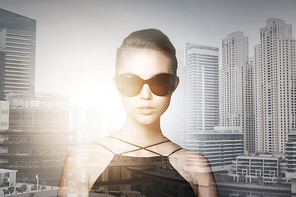 accessories, eyewear, fashion, people and luxury concept - beautiful young woman in elegant black sunglasses over dubai city with double exposure background