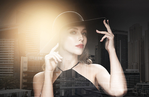 people, luxury and fashion concept - beautiful woman in black hat over dark over dubai city background with double exposure and highlight