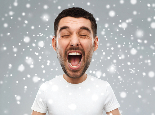 emotions, stress, winter, christmas and people concept - crazy shouting man in white t-shirt over snow on gray background (funny cartoon style character with big head)