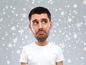 emotion, facial expression, winter, christmas and people concept - sad young man in white t-shirt looking up over snow on gray background (funny cartoon style character with big head)