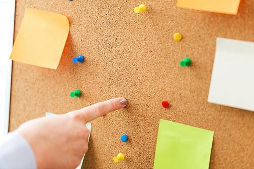 office, business, people and education concept - close up of hand pointing to to cork board with stickers and office pins
