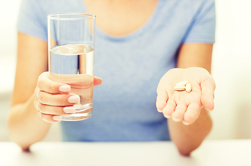 healthy eating, medicine, health care, food supplements and people concept - close up of woman hands holding pills and water glass at home