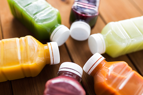 healthy eating, drinks, diet and detox concept - close up of plastic bottles with different fruit or vegetable juices on wooden table