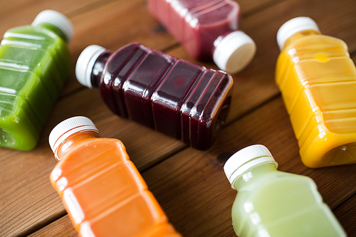 healthy eating, drinks, diet and detox concept - close up of plastic bottles with different fruit or vegetable juices on wooden table