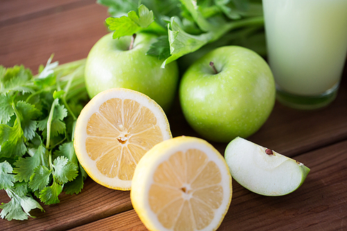 healthy eating, food, dieting and vegetarian concept - close up of lemons with apples, celery and green juice on wooden table