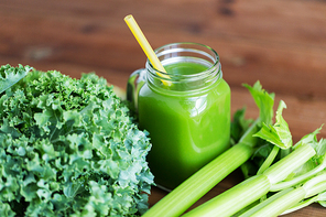 healthy eating, food, dieting and vegetarian concept - glass jug or mug with vegetable green juice, greens and celery on wooden table