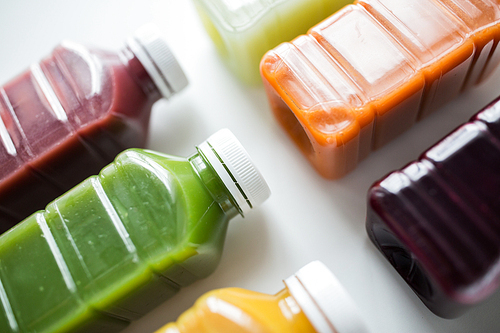 healthy eating, drinks, diet and detox concept - close up of plastic bottles with different fruit or vegetable juices on white