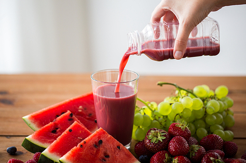 healthy eating, food, dieting and vegetarian concept - close up of hand pouring fruit and berry juice or smoothie from bottle to glass