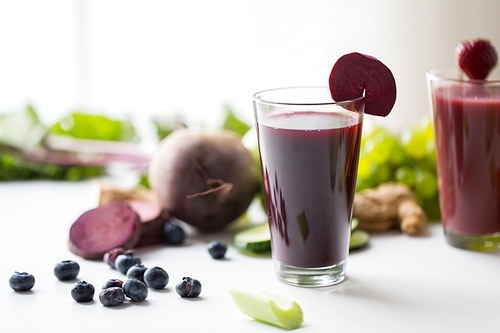 healthy eating, drinks,  and detox concept - glass of beetroot juice with different fruits and vegetables on table