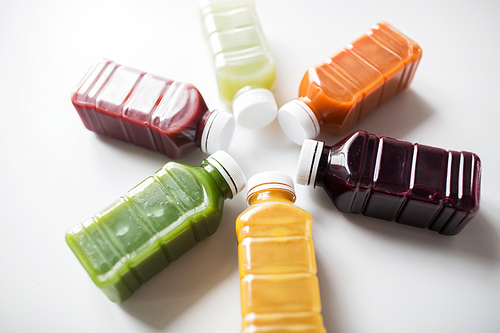 healthy eating, drinks,  and detox concept - close up of plastic bottles with different fruit or vegetable juices on white