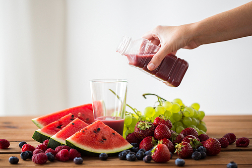 healthy eating, food, dieting and vegetarian concept - hand pouring fruit and berry juice or smoothie from bottle to glass