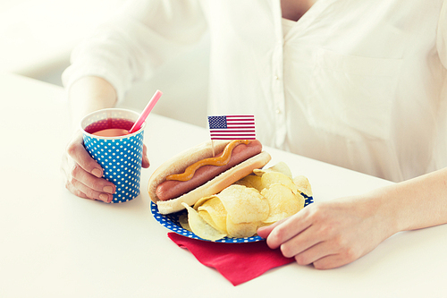독립기념일, celebration, patriotism and holidays concept - close up of woman eating hot dog with american flag decoration and potato chips, drinking juice and celebrating 4th july at home party