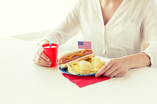 독립기념일, celebration, patriotism and holidays concept - close up of woman eating hot dog with american flag decoration and potato chips, drinking juice and celebrating 4th july at home party