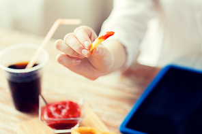 fast food, people and unhealthy eating concept - close up of woman dipping french fries into ketchup and drinking cola on wooden table