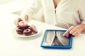 people, junk food, diet, technology and unhealthy eating concept - close up of hands with tablet pc computer and donuts counting calories and sitting at table at home