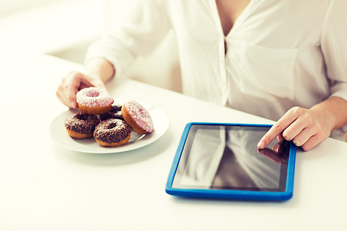 people, junk food, , technology and unhealthy eating concept - close up of hands with tablet pc computer and donuts counting calories and sitting at table at home
