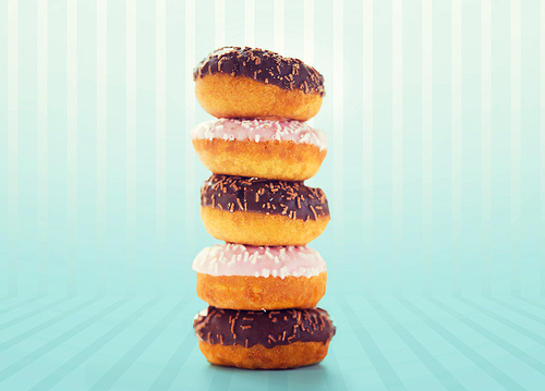 food, junk-food and eating concept - close up of glazed donuts pile over blue striped background
