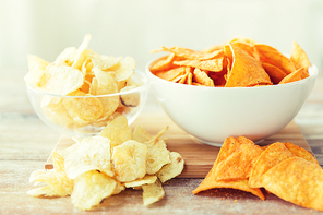 fast food, junk-food, cuisine and eating concept - close up of crunchy potato crisps and corn crisps or nachos in bowls