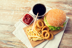 fast food and unhealthy eating concept - close up of hamburger or cheeseburger, deep-fried squid rings, french fries, cola drink and ketchup on wooden table