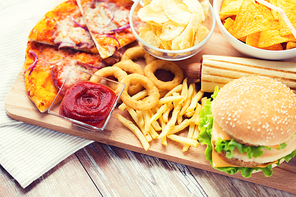 fast food and unhealthy eating concept - close up of hamburger or cheeseburger, deep-fried squid rings, french fries, pizza and ketchup on wooden table top view