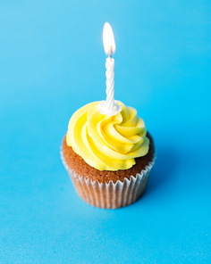 holiday, celebration, greeting and party concept - birthday cupcake with one burning candle over blue background