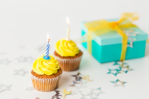 holiday, celebration, greeting and party concept - birthday cupcakes with burning candles and present