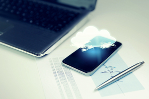 business, technology and information concept - close up of smartphone with cloud computing icon projection, laptop computer and chart with pen on office table