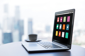 technology, media, business and modern life concept- close up of open laptop with computer menu icons on screen and coffee cup on table at office or hotel room