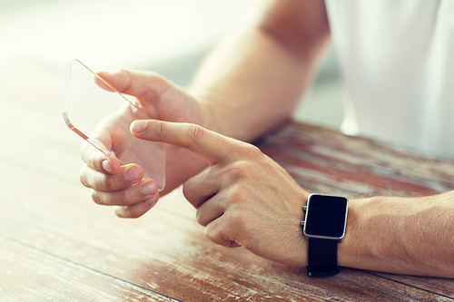 business, technology and people concept - close up of male hand holding and showing transparent smart phone and watch at home
