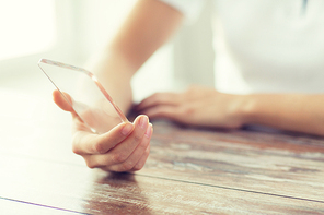 business, technology and people concept - close up of woman hand holding and showing transparent smartphone at home