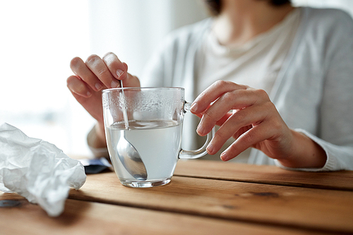 healthcare, medicine and people concept - close up of woman stirring medication in cup with spoon