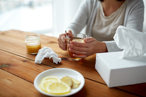 health, traditional medicine and ethnoscience concept - ill woman drinking tea with lemon and honey and paper wipes box on wooden table