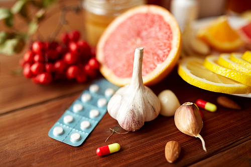healthcare, traditional medicine, flu and ethnoscience concept - garlic and pills on wooden table