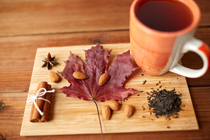 autumn and season concept - cup of tea, maple leaf and almond on wooden board