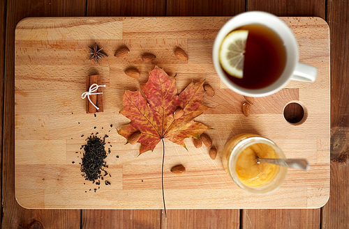 autumn and ethnoscience concept - cup of lemon tea and honey on wooden board with maple leaf and almond