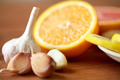 health, food, cooking, traditional medicine and ethnoscience concept - close up of garlic and orange on wooden table